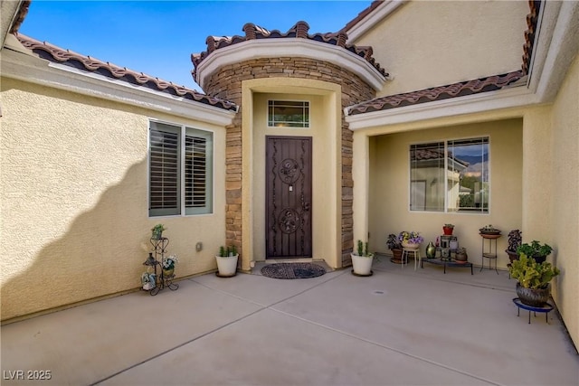 property entrance with a patio area, stucco siding, and stone siding