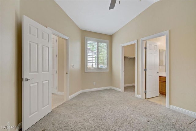 unfurnished bedroom featuring baseboards, light carpet, vaulted ceiling, and a spacious closet