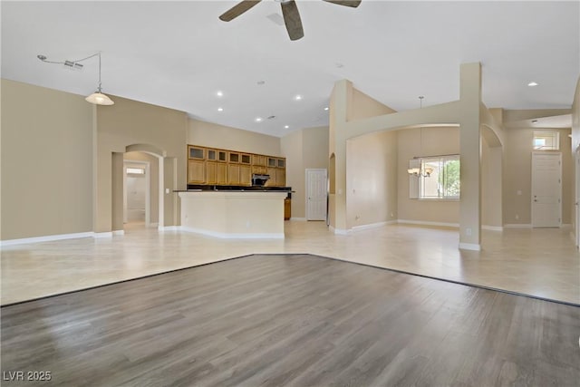 unfurnished living room featuring ceiling fan, light wood finished floors, arched walkways, baseboards, and visible vents