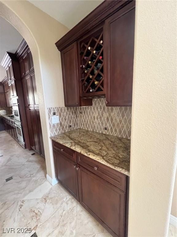 bar with backsplash, arched walkways, and marble finish floor