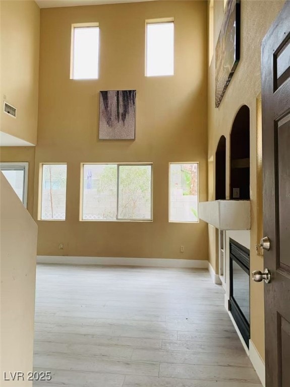 unfurnished living room featuring a towering ceiling, visible vents, wood finished floors, baseboards, and a glass covered fireplace