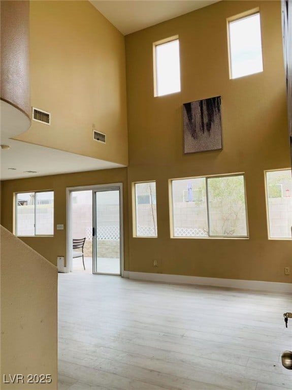 unfurnished living room featuring a towering ceiling, light wood-type flooring, and visible vents