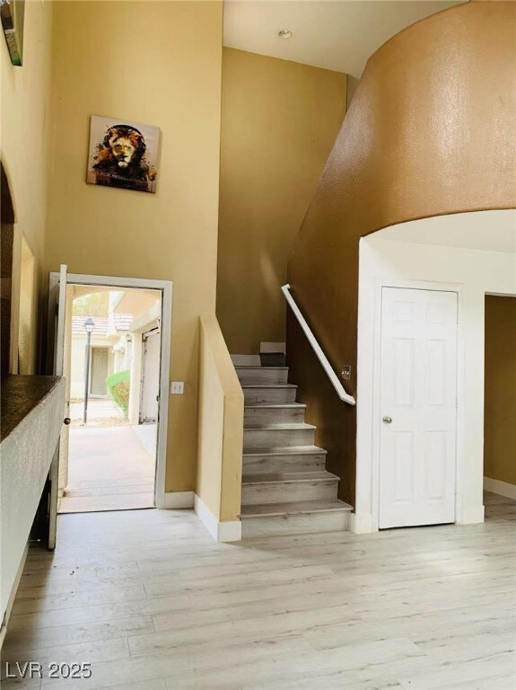 staircase featuring baseboards, wood finished floors, and a towering ceiling