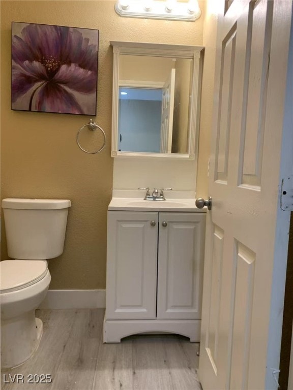 bathroom featuring toilet, baseboards, wood finished floors, and vanity