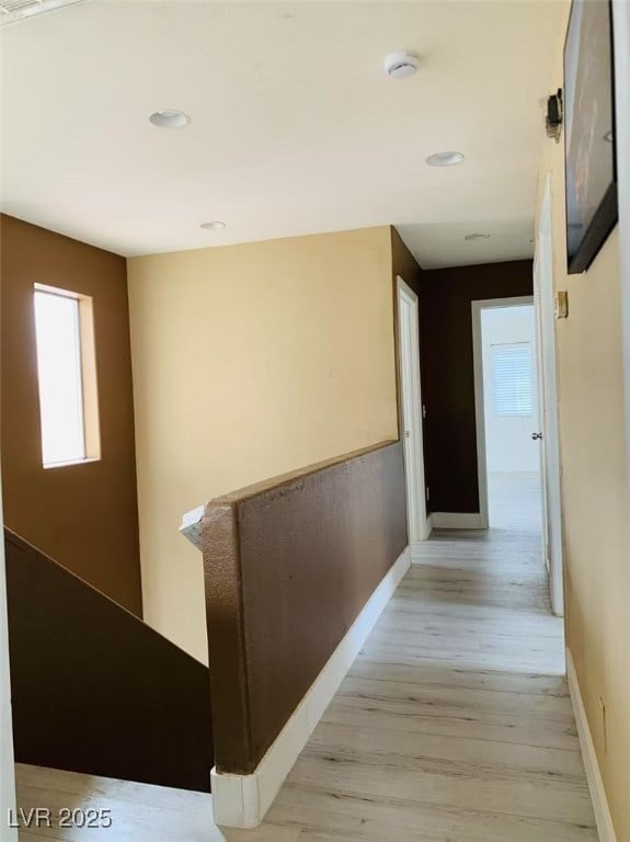 hall with light wood-style floors, baseboards, and a healthy amount of sunlight
