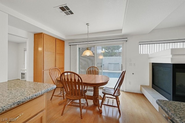 dining area featuring visible vents, a glass covered fireplace, a raised ceiling, and light wood-type flooring