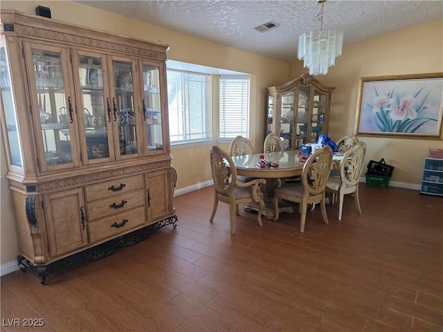 dining space with a textured ceiling, a chandelier, baseboards, dark wood-type flooring, and visible vents