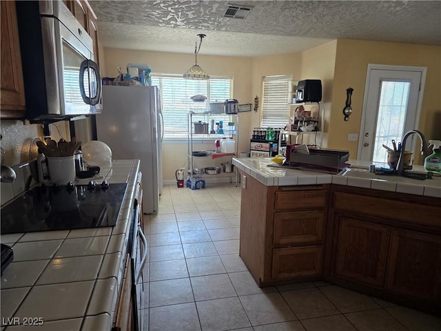kitchen featuring tile counters, stainless steel microwave, visible vents, and a healthy amount of sunlight
