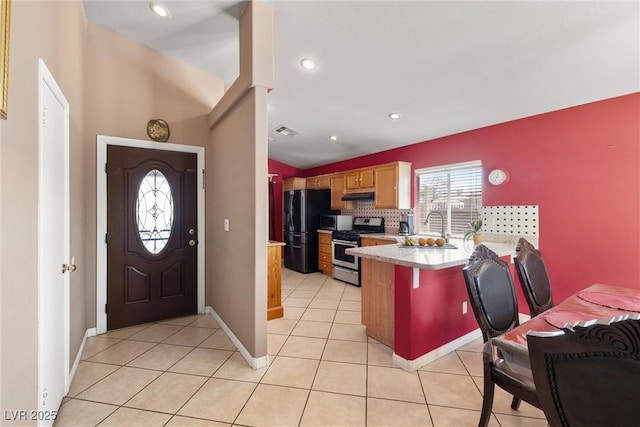 kitchen with gas stove, light countertops, freestanding refrigerator, a peninsula, and under cabinet range hood