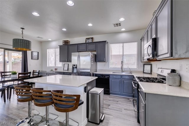 kitchen featuring visible vents, a kitchen island, light wood-type flooring, a sink, and appliances with stainless steel finishes