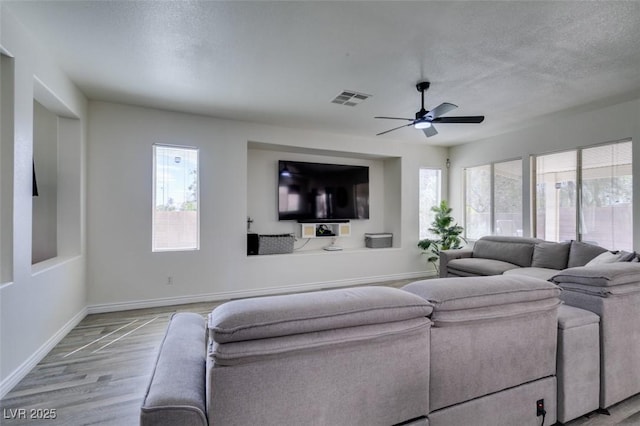 living room featuring a textured ceiling, baseboards, visible vents, and ceiling fan