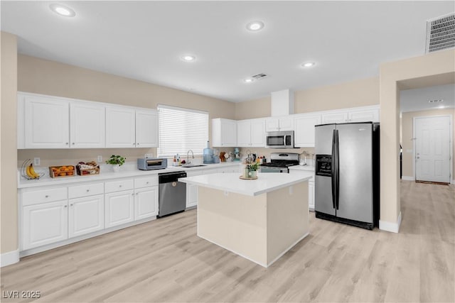 kitchen with stainless steel appliances, light wood finished floors, light countertops, white cabinets, and a kitchen island