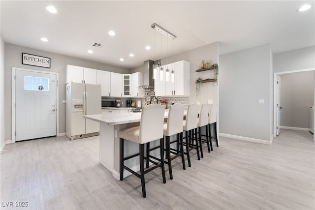 kitchen with wall chimney range hood, a breakfast bar area, light wood-style flooring, white fridge with ice dispenser, and a peninsula