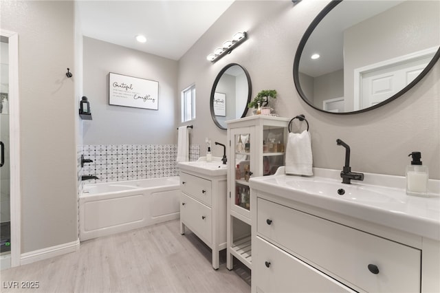 bathroom featuring a garden tub, wood finished floors, two vanities, a shower stall, and a sink