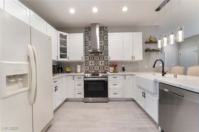 kitchen with wall chimney range hood, backsplash, appliances with stainless steel finishes, a sink, and recessed lighting