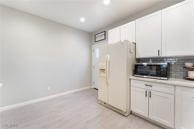 kitchen with white cabinets, white refrigerator with ice dispenser, light wood-style flooring, stainless steel microwave, and tasteful backsplash