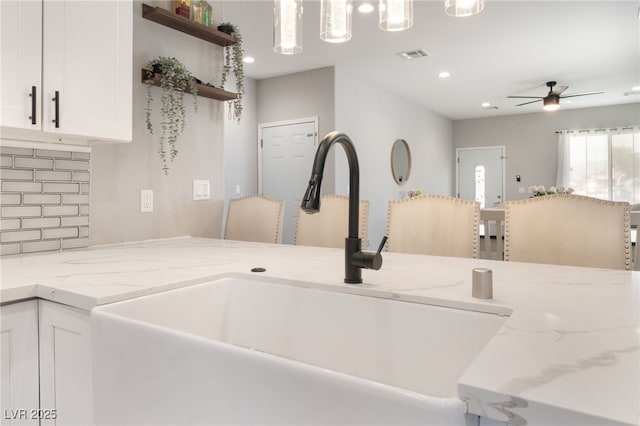 kitchen featuring ceiling fan, visible vents, light stone countertops, a sink, and white cabinets