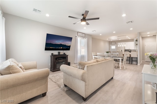 living room featuring light wood-style floors, a ceiling fan, visible vents, and recessed lighting