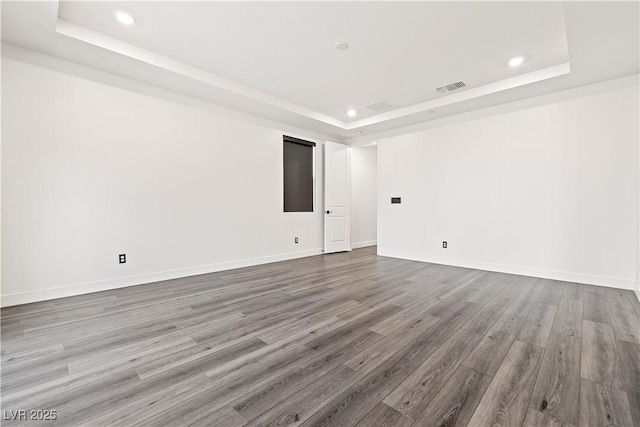 unfurnished room with visible vents, recessed lighting, a raised ceiling, and wood finished floors