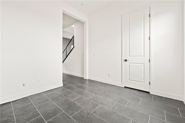 unfurnished room with dark tile patterned flooring, baseboards, and stairway