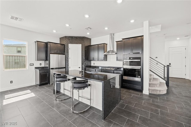 kitchen featuring wall chimney range hood, a kitchen bar, visible vents, dark tile patterned flooring, and stainless steel appliances