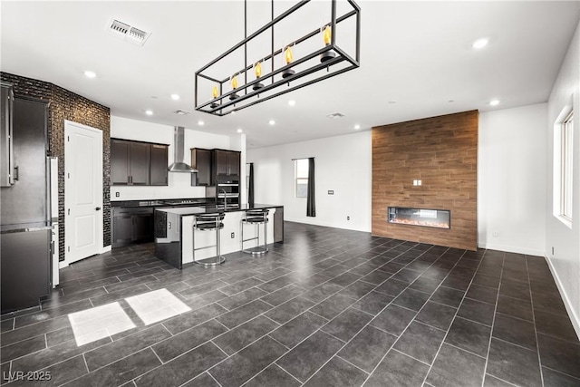 kitchen with wall chimney range hood, dark countertops, recessed lighting, open floor plan, and visible vents