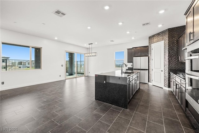 kitchen with appliances with stainless steel finishes, visible vents, a center island with sink, and a sink