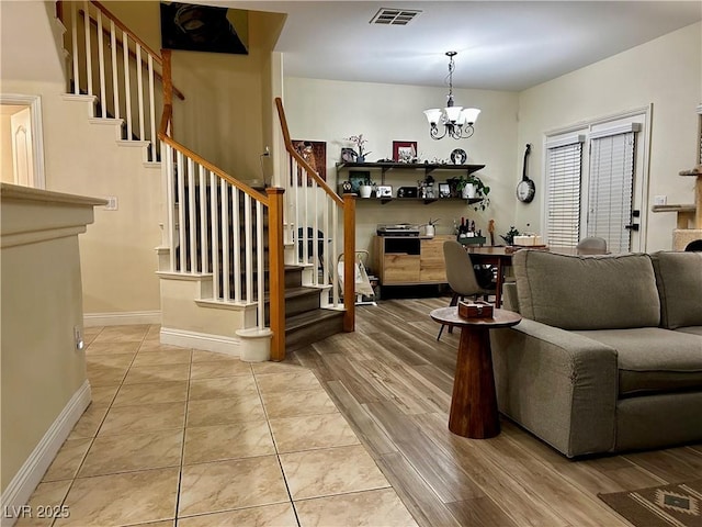living area featuring a chandelier, baseboards, visible vents, and stairway