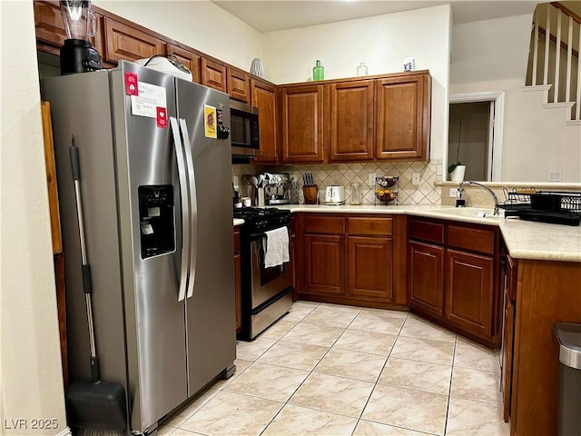 kitchen featuring appliances with stainless steel finishes, a sink, light countertops, brown cabinetry, and decorative backsplash