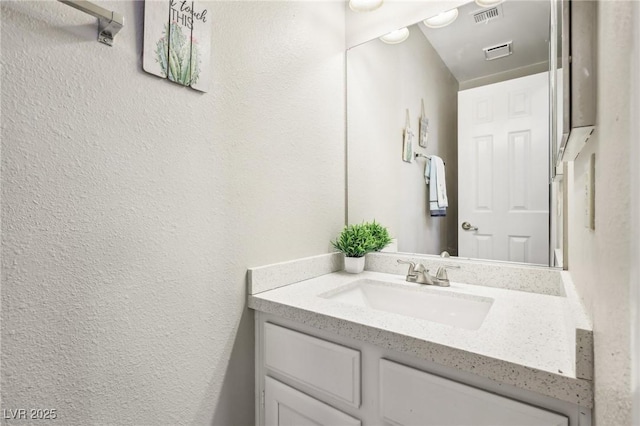 bathroom featuring a textured wall, visible vents, and vanity