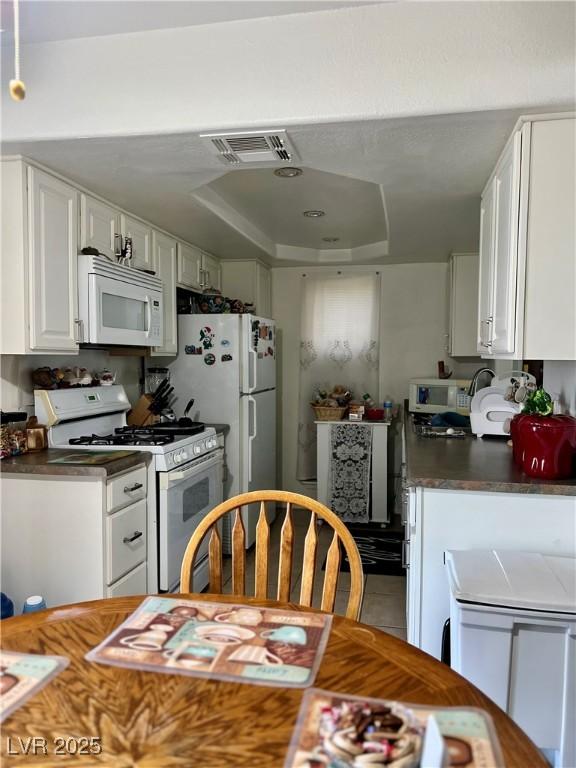 1440 Vegas Valley Dr Unit 2, Las Vegas, NV 89169 - kitchen with visible vents, dark countertops, white cabinets, a tray ceiling, and white appliances