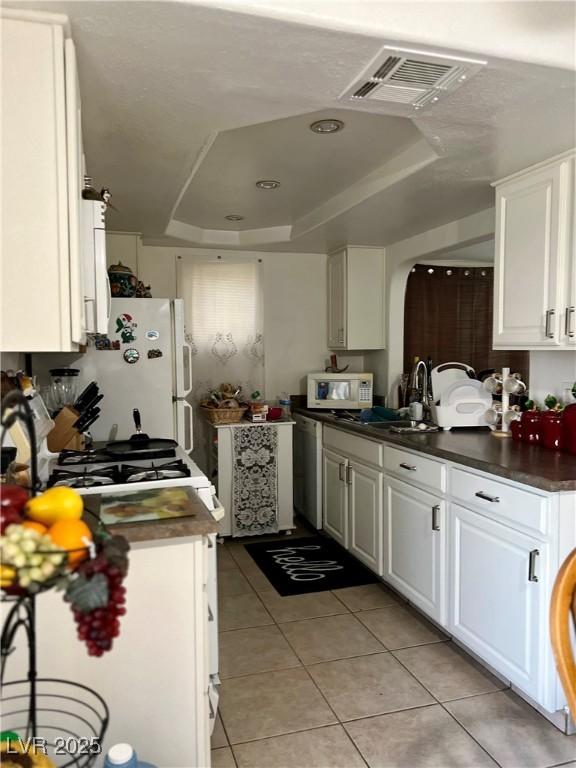 1440 Vegas Valley Dr Unit 2, Las Vegas, NV 89169 - kitchen featuring dark countertops, white appliances, light tile patterned floors, a tray ceiling, and visible vents