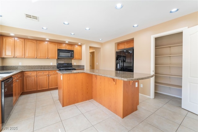 kitchen featuring light tile patterned flooring, light stone counters, a breakfast bar, a center island, and black appliances
