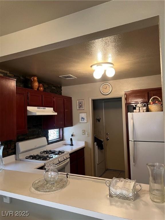 kitchen with dark brown cabinets, white appliances, light countertops, under cabinet range hood, and visible vents