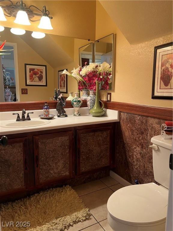 bathroom featuring tile patterned flooring, vanity, wainscoting, toilet, and vaulted ceiling