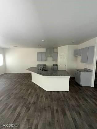 4645 Fuchsia Nights Ave Unit 103, North Las Vegas, NV 89084 - kitchen featuring gray cabinetry, dark countertops, an island with sink, and dark wood finished floors