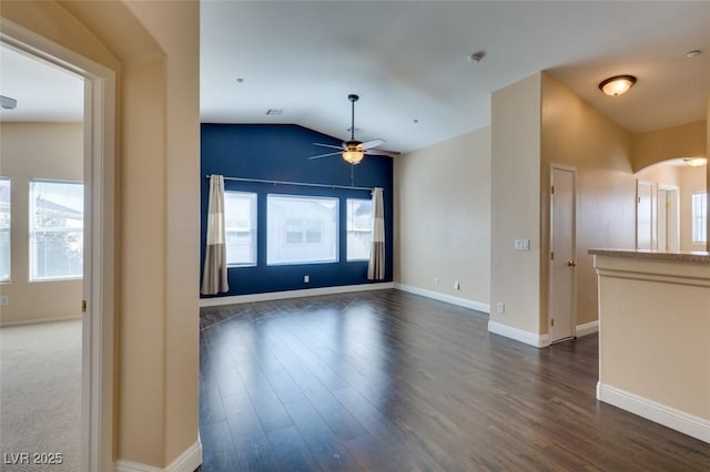 unfurnished room featuring a ceiling fan, arched walkways, dark wood finished floors, and vaulted ceiling