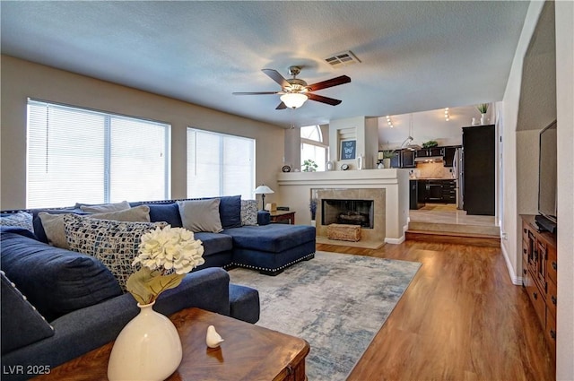 living area with a ceiling fan, a textured ceiling, visible vents, a fireplace, and light wood-style floors