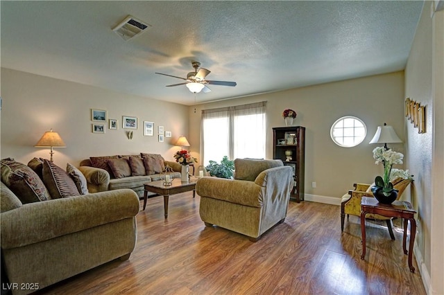 living room with visible vents, baseboards, ceiling fan, dark wood-type flooring, and a textured ceiling