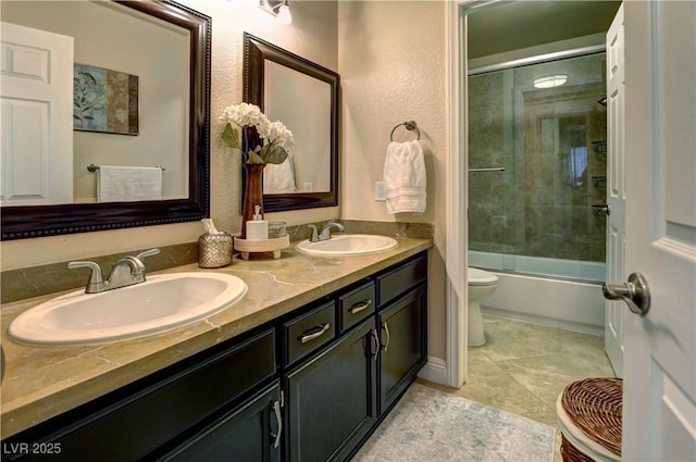 bathroom featuring double vanity, toilet, a sink, and bath / shower combo with glass door