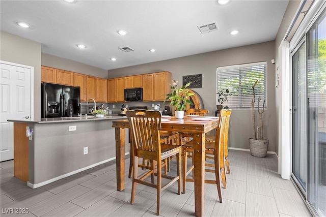 kitchen featuring black appliances, recessed lighting, light countertops, baseboards, and a center island with sink