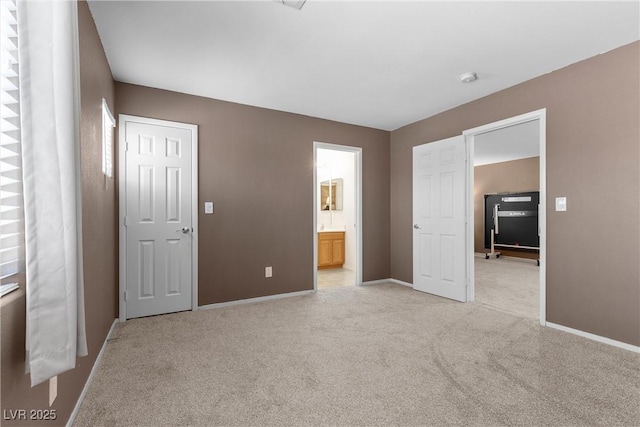 unfurnished bedroom featuring light carpet, baseboards, and ensuite bath