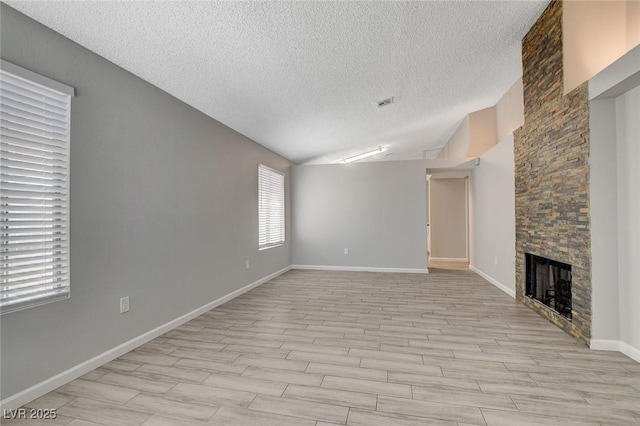 unfurnished living room with lofted ceiling, a stone fireplace, baseboards, light wood-style floors, and a textured ceiling
