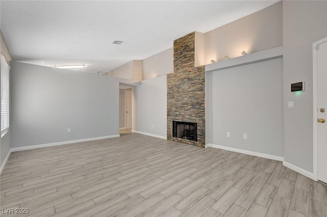 unfurnished living room featuring a textured ceiling, a stone fireplace, baseboards, high vaulted ceiling, and light wood-style floors