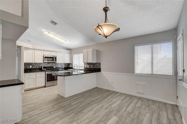 kitchen featuring wainscoting, a peninsula, white cabinetry, a sink, and appliances with stainless steel finishes