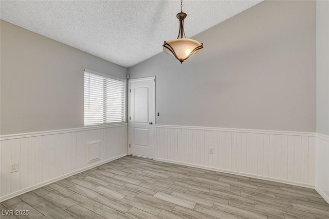 empty room with a textured ceiling, wood finished floors, and a wainscoted wall