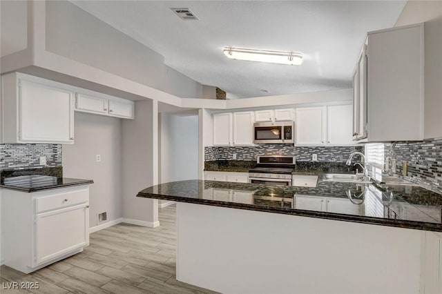kitchen with decorative backsplash, a peninsula, a sink, dark stone countertops, and appliances with stainless steel finishes