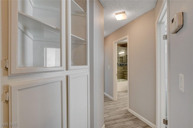 hallway with a textured ceiling, baseboards, and light wood finished floors