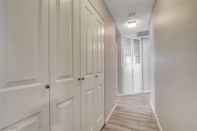 corridor featuring a textured ceiling, baseboards, visible vents, and light wood-style floors