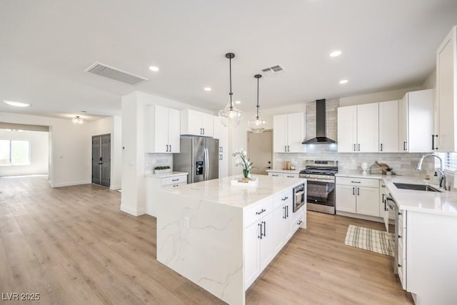 kitchen featuring visible vents, a sink, wall chimney range hood, and stainless steel appliances